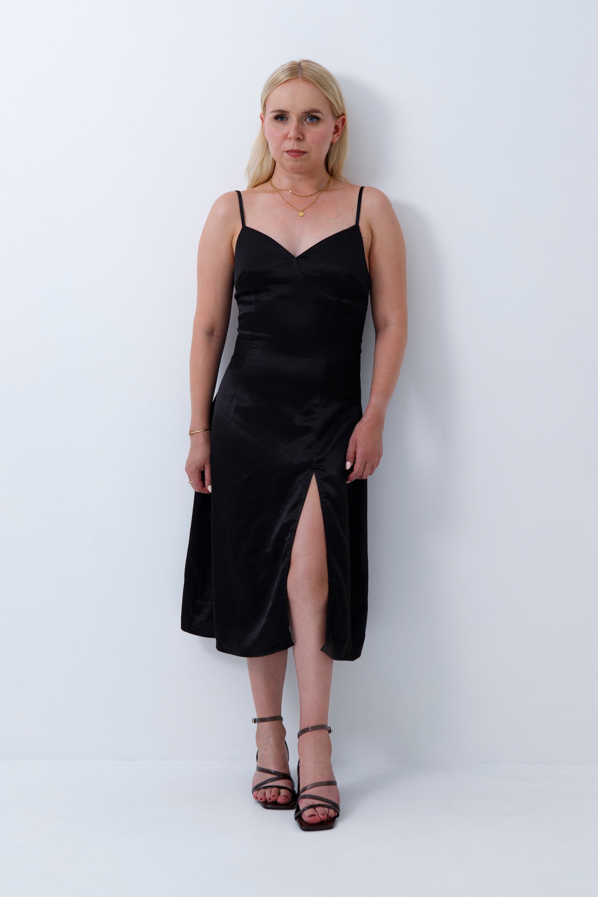Petite woman wearing a petite black slip dress against a white background