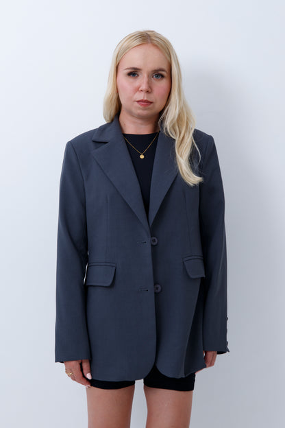 A woman wearing grey oversized blazer for petites on a white background