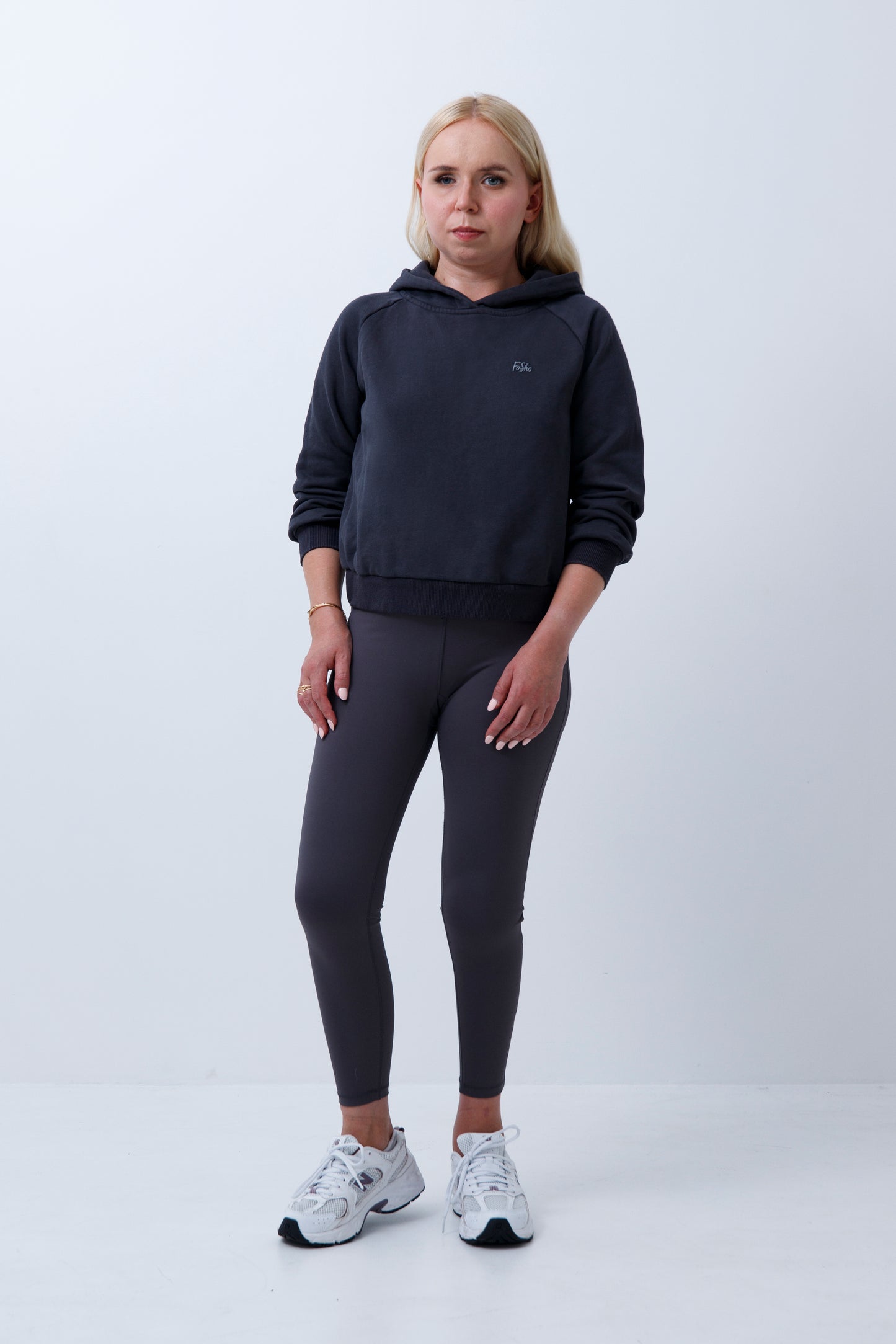 A woman wearing dark grey hoodie and leggings on a white background