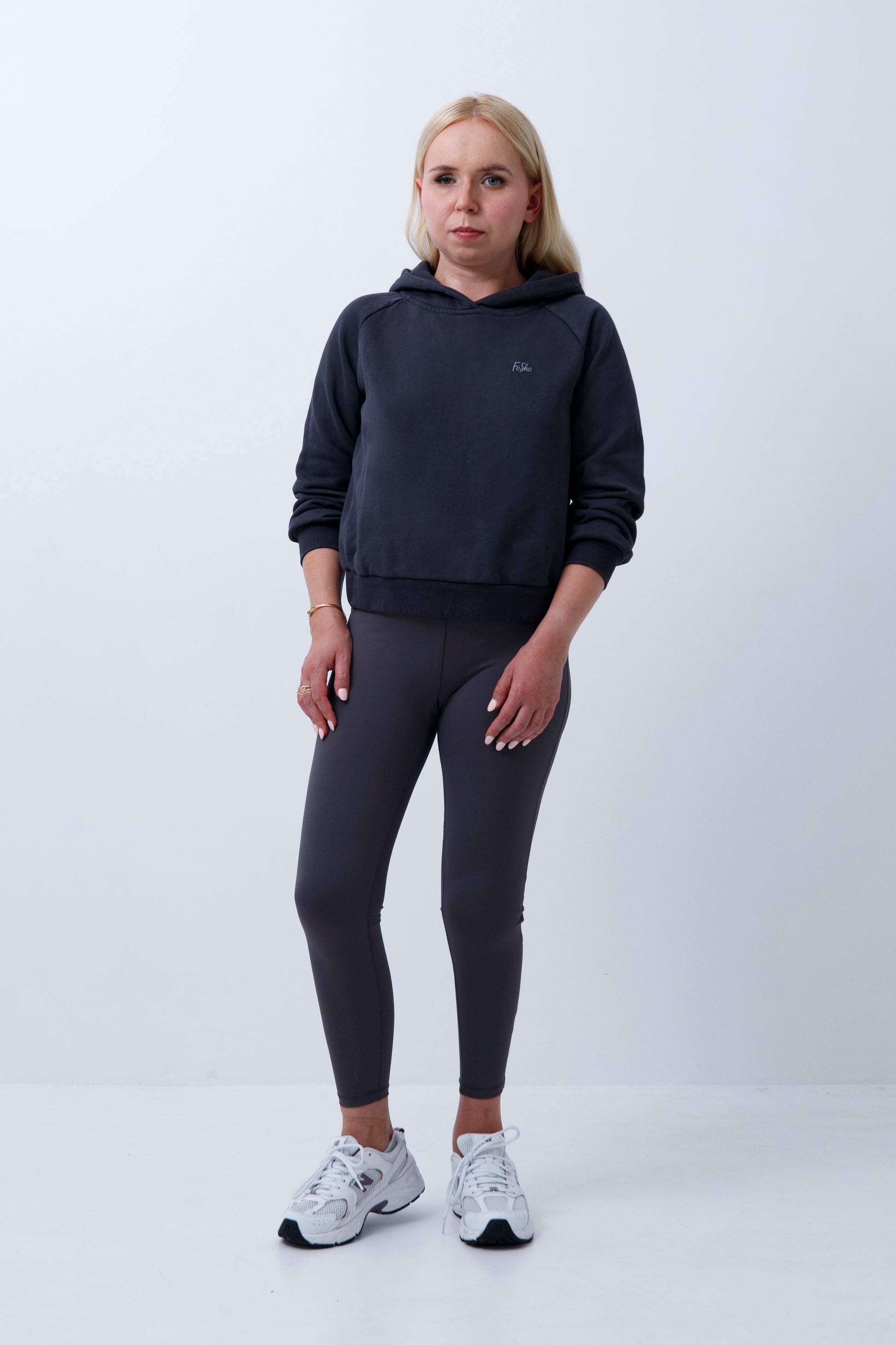 A woman wearing dark grey hoodie and leggings on a white background