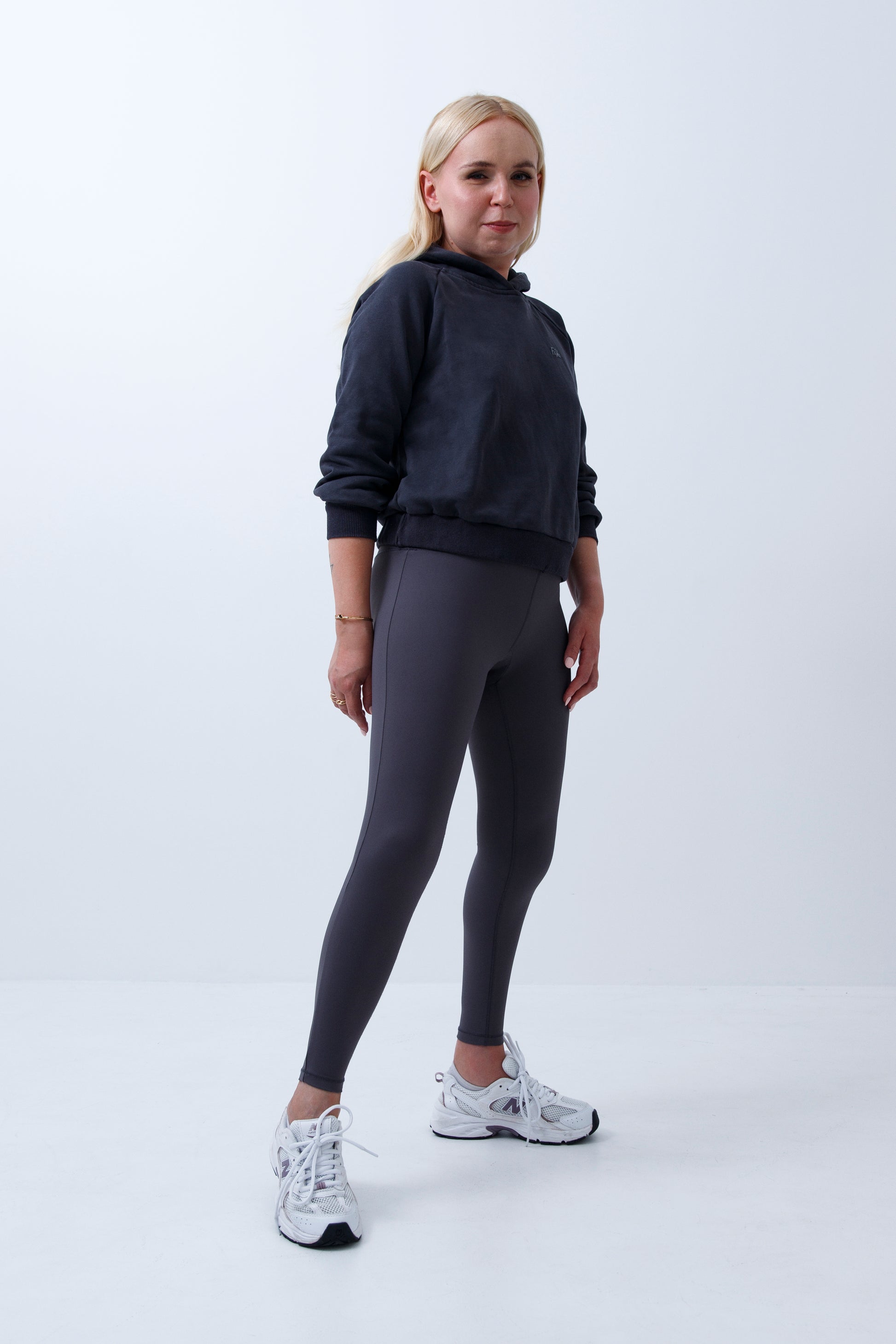 A woman wearing dark grey hoodie and leggings on a white background