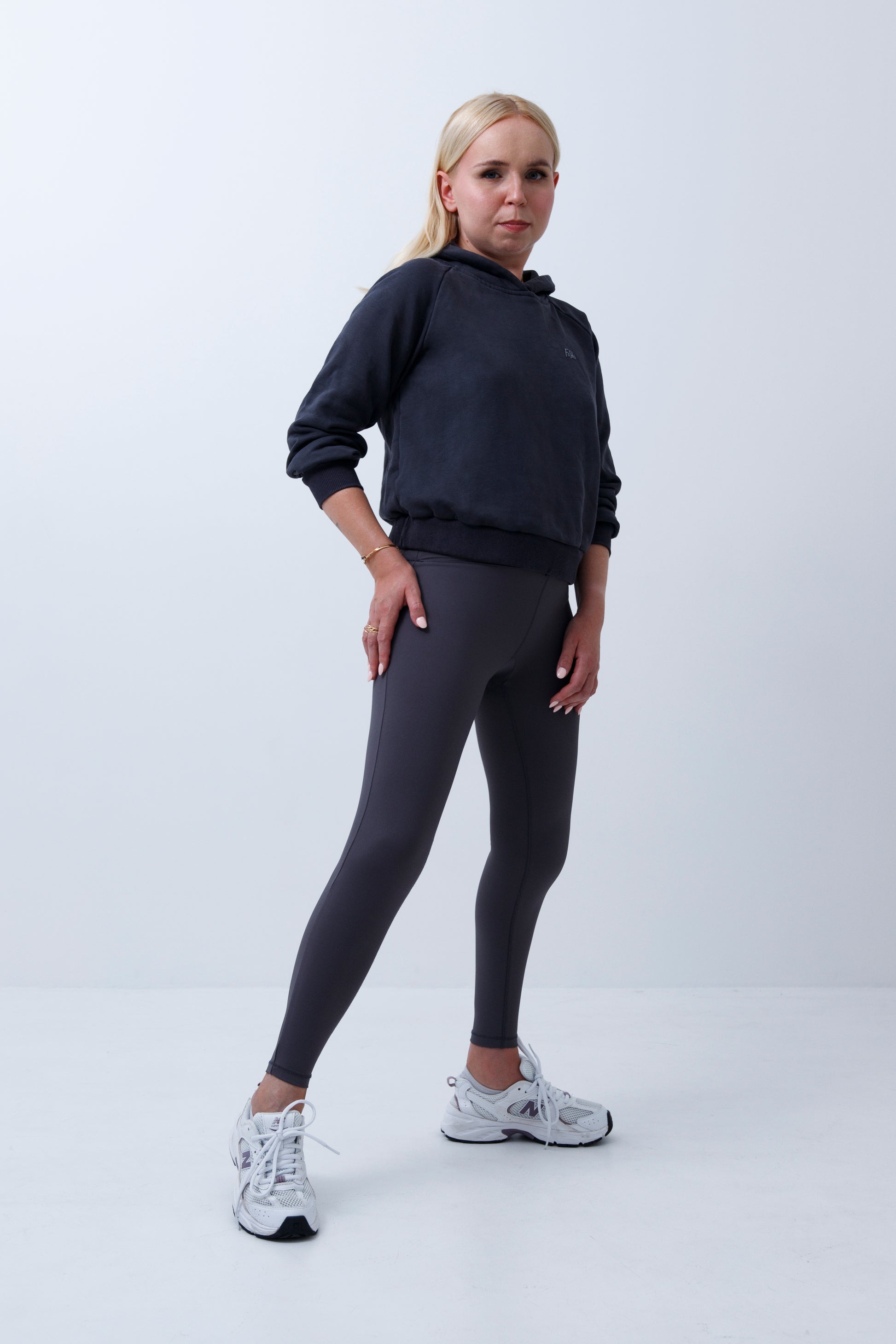 A woman wearing dark grey hoodie and leggings on a white background
