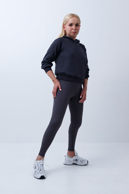 A woman wearing dark grey hoodie and leggings on a white background
