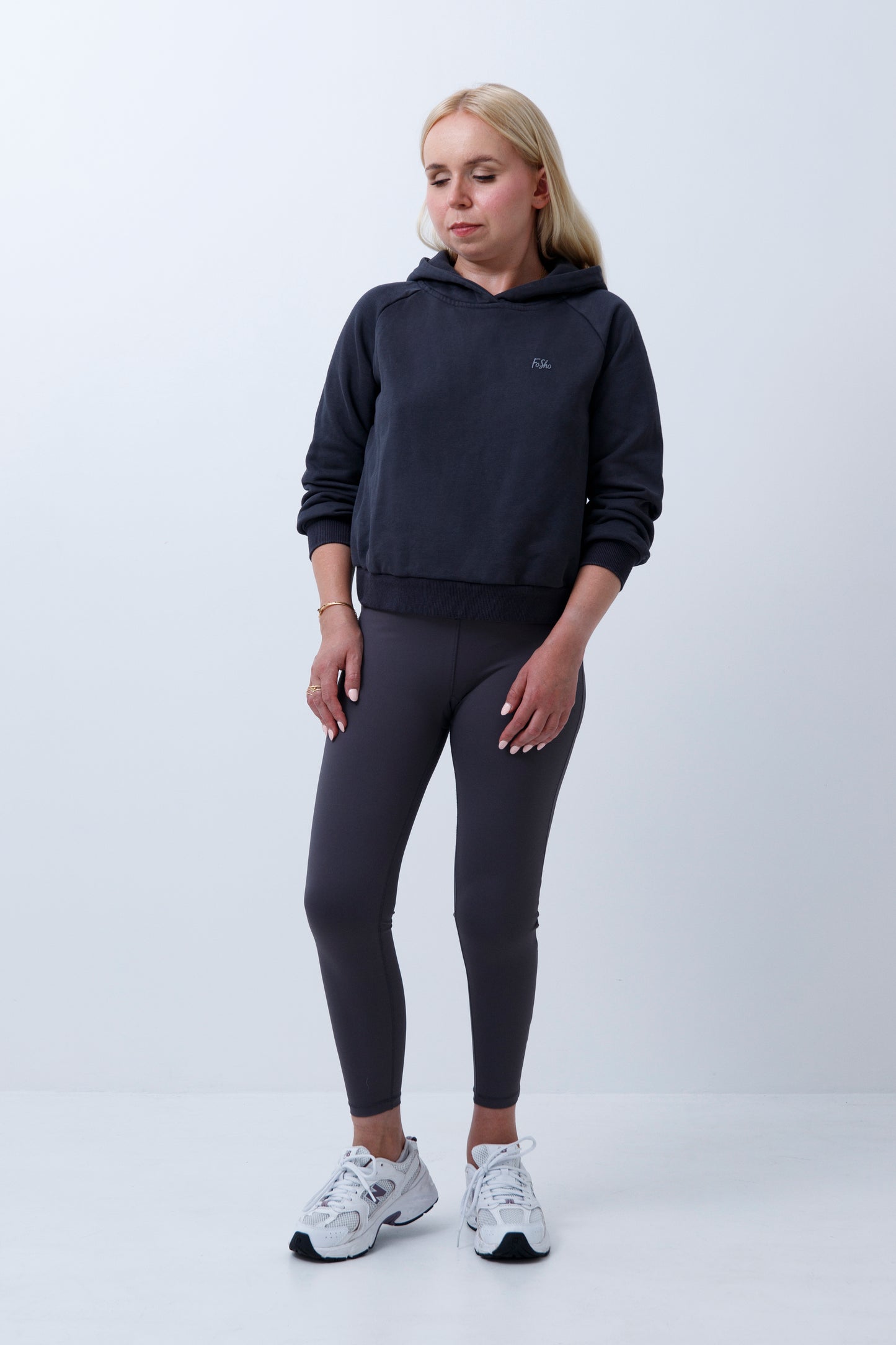 A woman wearing dark grey hoodie and leggings on a white background
